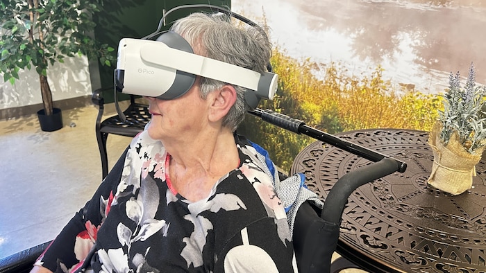 Une femme âgée dans un fauteuil roulant avec un casque de réalité virtuelle sur la tête.