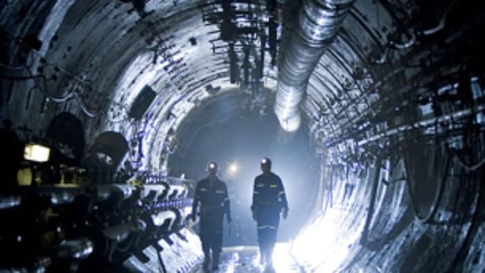 Deux hommes marchent dans un tunnel de mine peu éclairé.