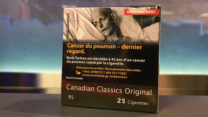 Un emballage de cigarettes neutre, dont 80 % est recouvert d'un avertissement montrant un mourant. Une fine bande brune apparaît au bas du paquet, avec les inscriptions de la marque et du nombre de cigarettes qu'il renferme.