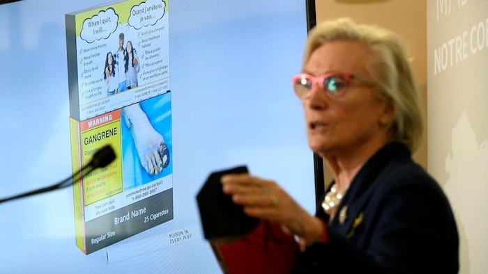 An example of cigarette packaging with expanded warnings, including a warning printed on the cigarettes themselves, is shown on a screen behind Minister of Mental Health and Addictions Carolyn Bennett at the University of Ottawa Heart Institute on June 10, 2022.