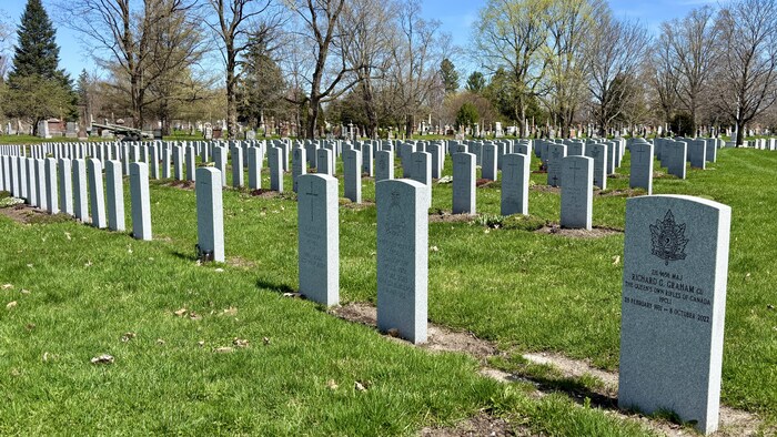 Plusieurs pierres tombales sont alignées dans un cimetière.