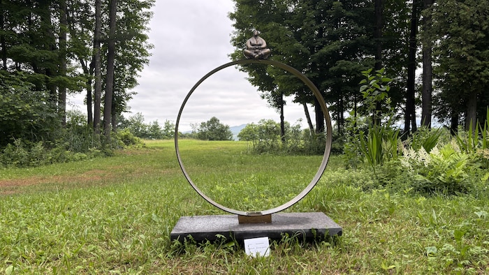 Une sculpture en forme d'anneau métallique sur laquelle est assise la silhouette d'une personne.