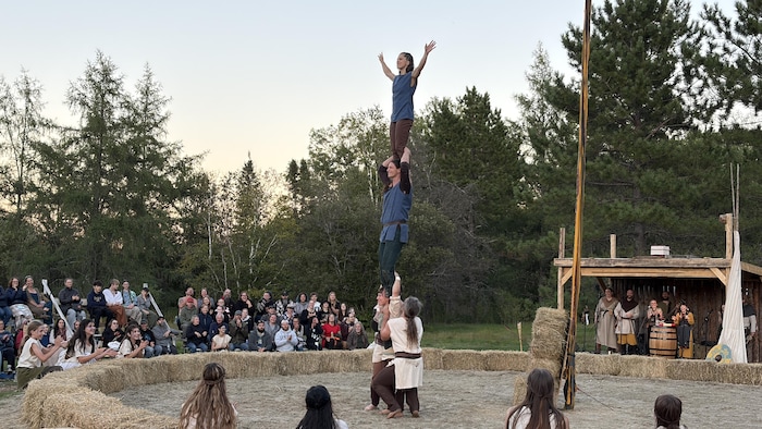 Une femme porte un homme sur ses épaules, qui porte lui-même une femme sur ses épaules lors d'un spectacle de cirque.