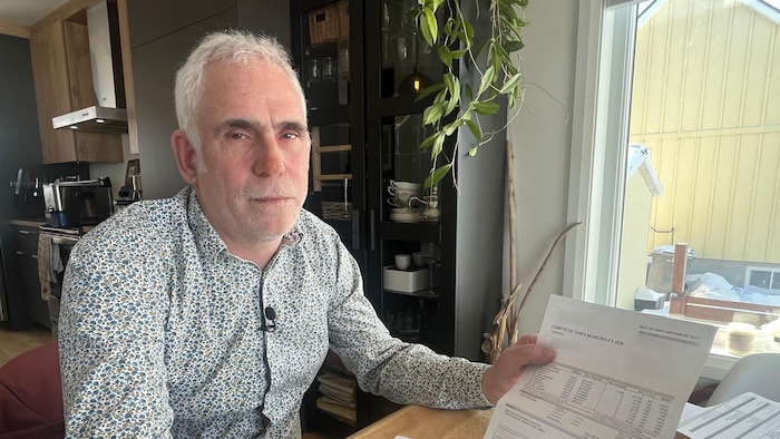 Un homme assis à sa table de cuisine avec son compte de taxes dans les mains.
