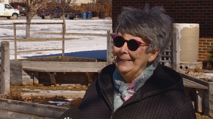 Une femme parle au micro devant un potager communautaire.