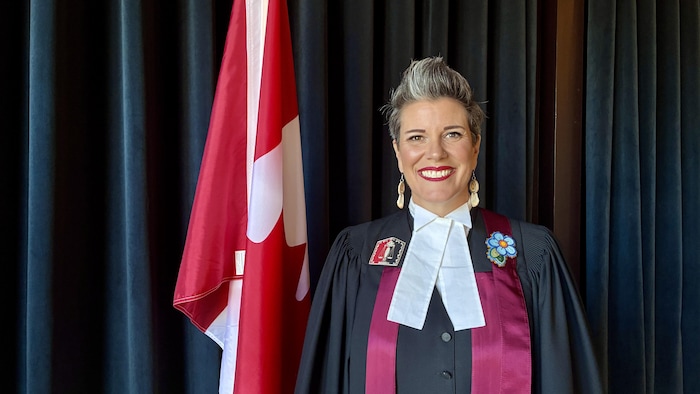 Suzanne Carrière, juge de la citoyenneté, posant à côté d'un drapeau canadien.