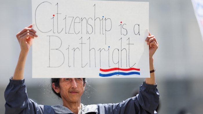 Une manifestante tient une pancarte qui dit : « La citoyenneté est un droit de naissance ». 