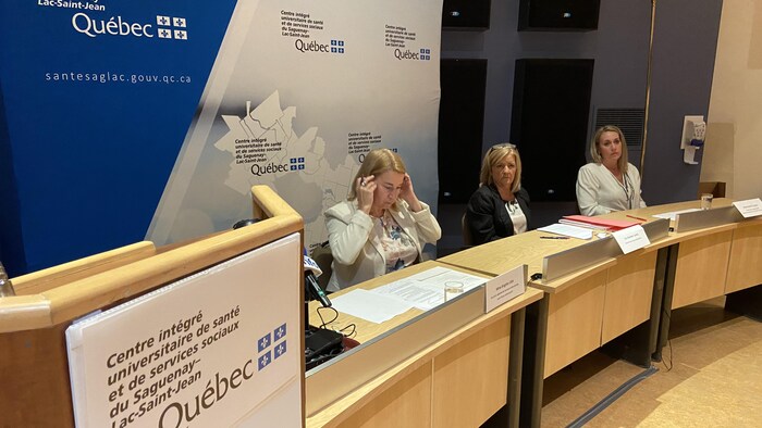 Trois personnes sont assises derrière des bureaux en demi-cercle.