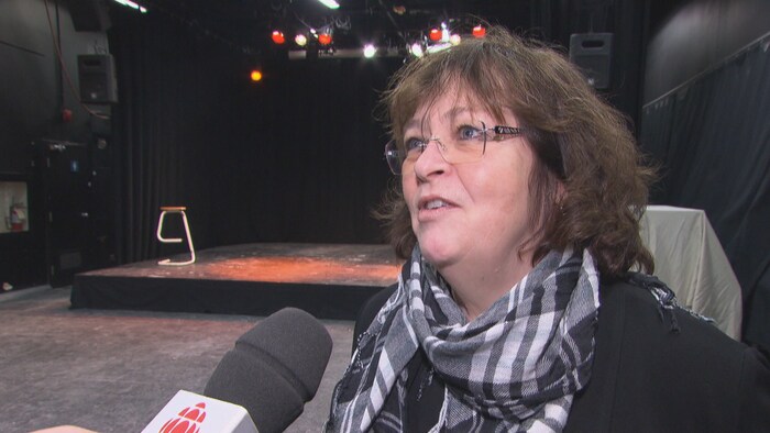 Une femme installée devant une scène est en entrevue et parle devant un micro de Radio-Canada.