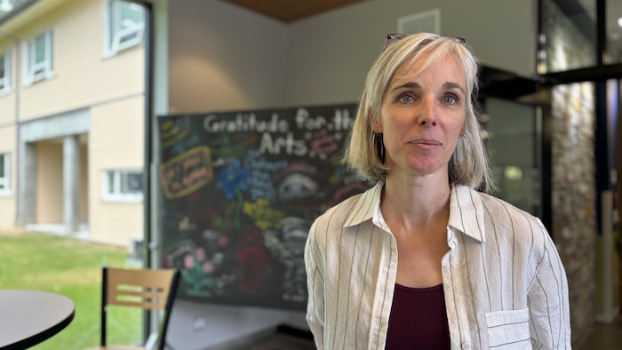 Une femme avec un tableau en arrière-plan avec des messages de gratitude de la part d'anciens étudiants. 
