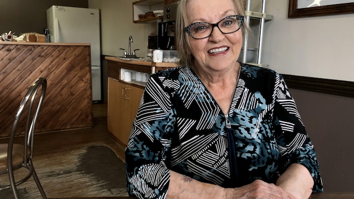 Claire Savard est assise à une table de son restaurant, elle sourit à la caméra.