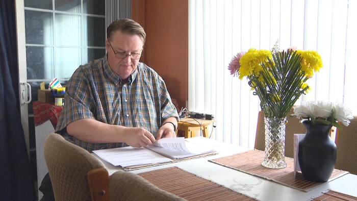 Un homme assis à une table de cuisine décorée d'un bouquet parcourt une pile de documents.