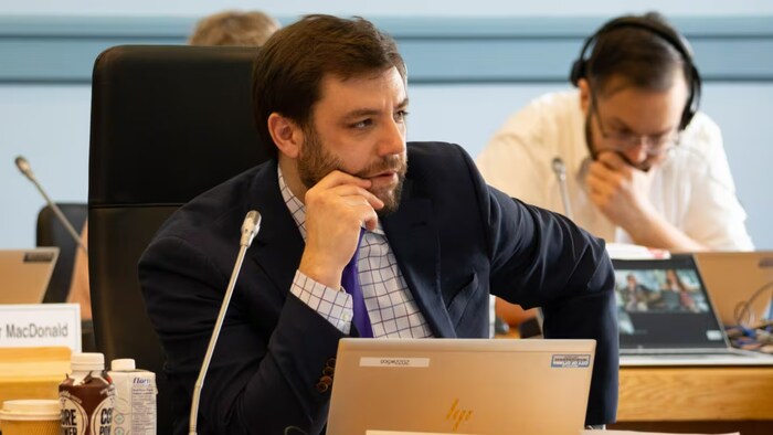 Le conseiller municipal du quartier West Carleton-March, Clarke Kelly, derrière un bureau et un micro. 