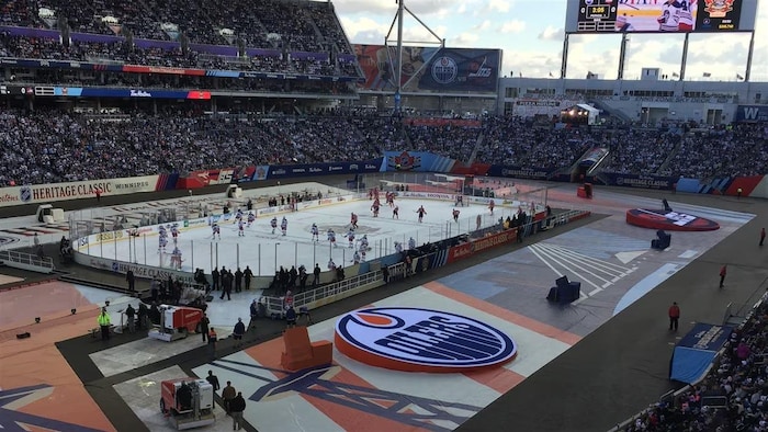 Des joueurs de hockey patinent sur une patinoire extérieure dans un stade.