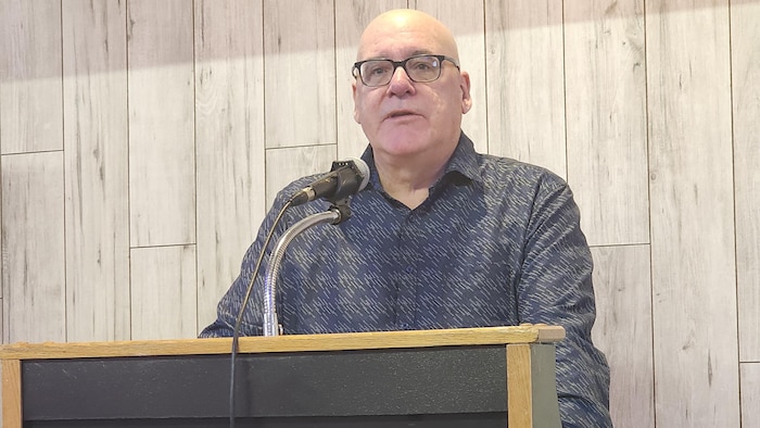 Claude Balleux debout derrière un pupitre.