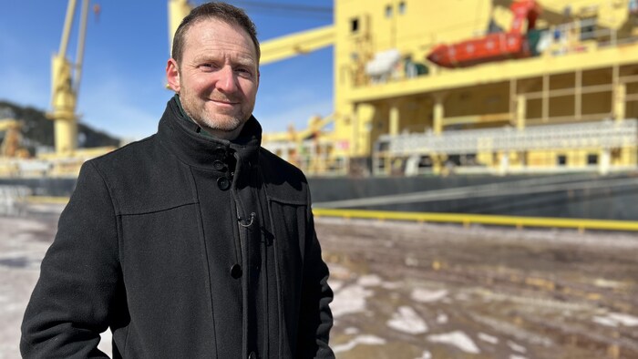 Un homme pose devant un bateau de marchandise au port de Saguenay.