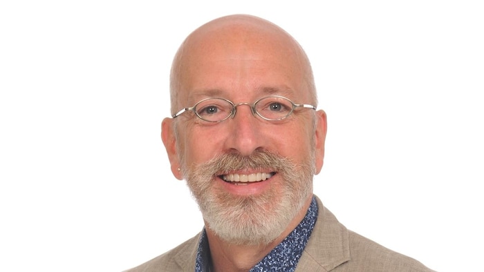 Claude Gagné qui sourit sur un fond blanc. 