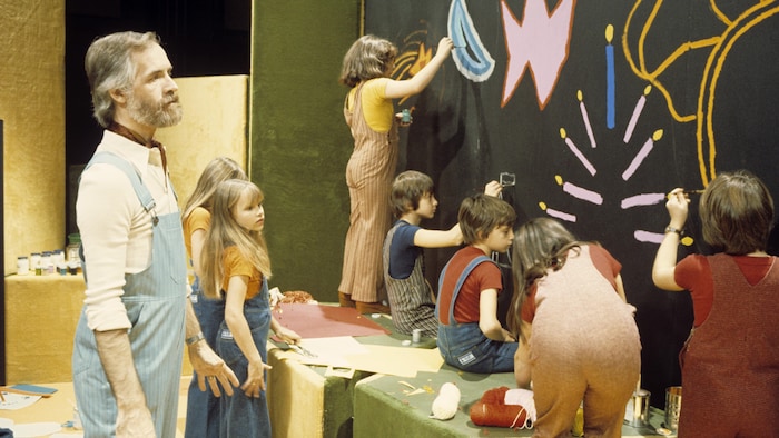 

Dans un studio de télévision, l'animateur Claude Lafortune surveille la progression de la réalisation d'une murale.