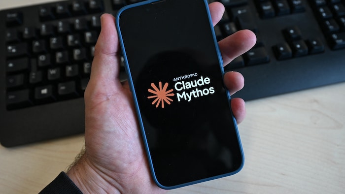 Une main tient un cellulaire sur lequel est affiché le logo de Claude Mythos.