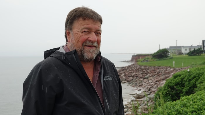 Claude Poirier photographié devant une côte enrochée.