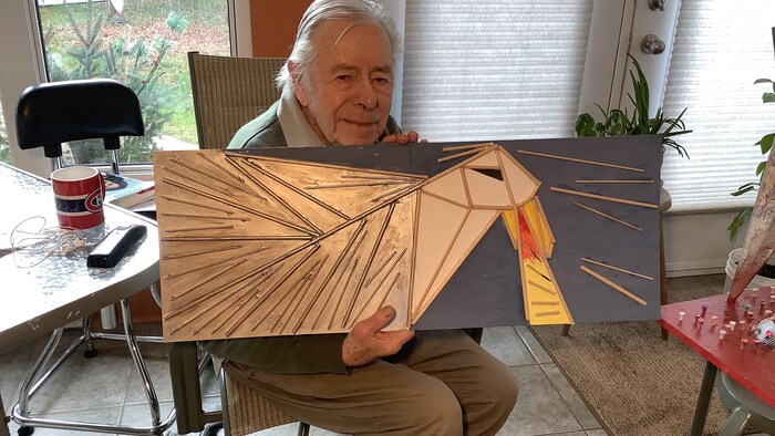 L'artiste visuel Claude Roussel a dans ses mains une toile représentant un aigle.