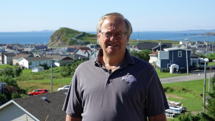 Claude Thériault, propriétaire de l’Auberge du port, devant un hameau de petites maison madeliniennes et la mer. 