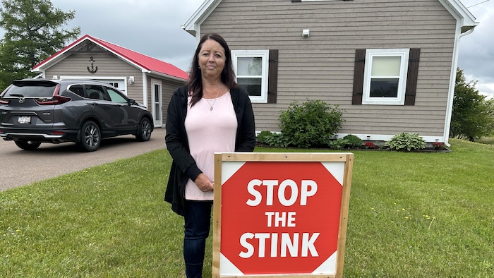 Claudette Robichaud devant un panneau qui dit « arrêtez les odeurs nauséabondes ».