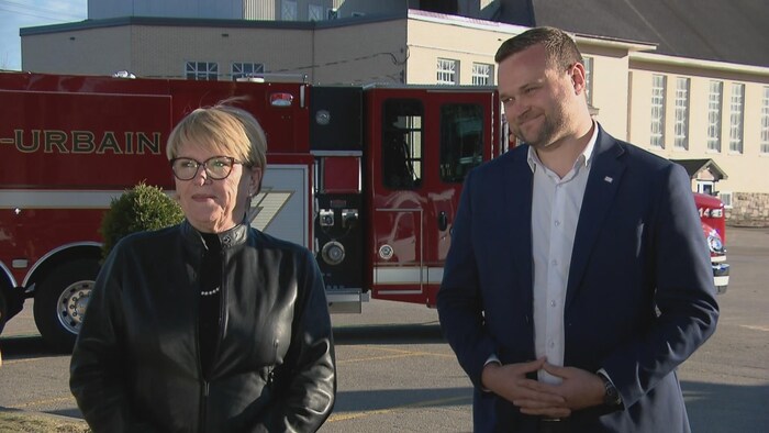 Une femme et un homme accordent une entrevue devant un camion de pompiers, à l'extérieur.
