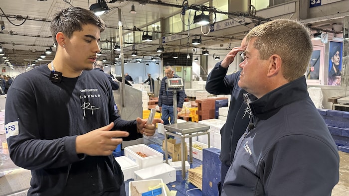 Deux hommes discutent dans un marché de poissons et de fruits de mer.