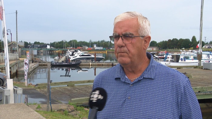 Un homme interviewé devant des bateaux de plaisance amarrés à des quais.