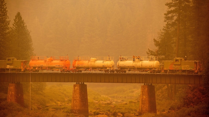 Un train de pompiers traversant un pont, dans un paysage saturé par les fumées d'incendies.