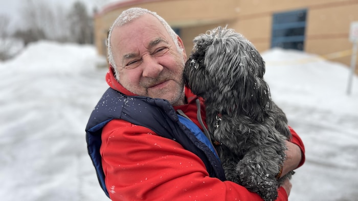 Un homme tient un petit chien dans ses bras, près de son visage.