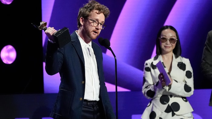 Un homme sur scène prononce un discours, trophée à la main.