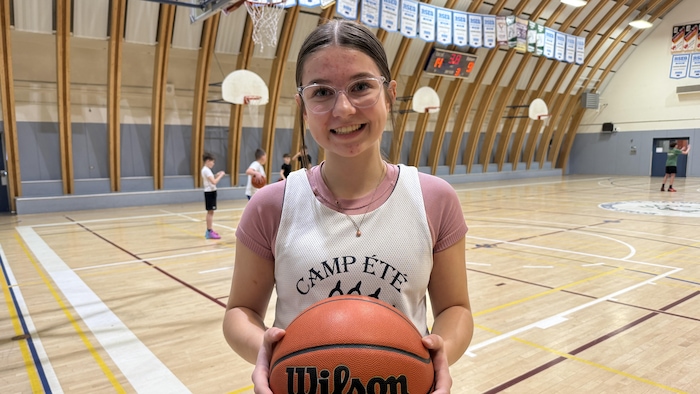 Une jeune fille tient un ballon de basdket en main. 