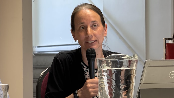 Sarah Charbonneau parle dans un micro, assise à une table à l'avant de la salle.