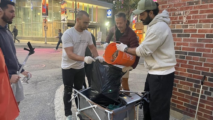 Un homme ouvre un sac de poubelle et un autre homme vide le contenu d'un seau à l'intérieur du sac.