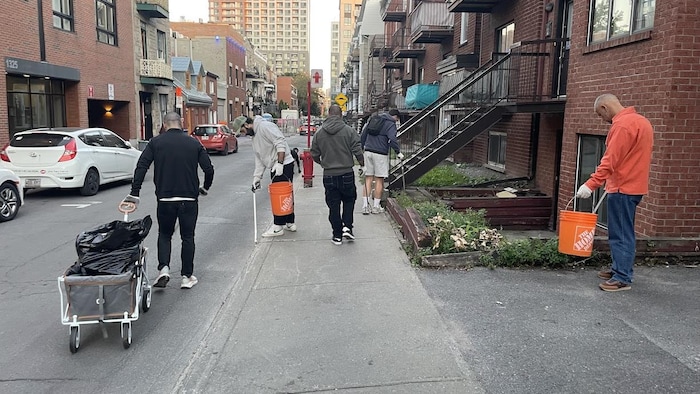 Cinq hommes ramassent des déchets dans la rue à l'aide de pinces métalliques.
