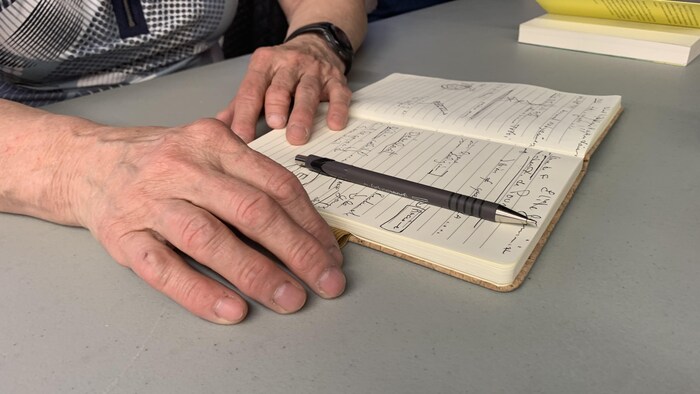 Des mains reposent sur une table à proximité d'un stylo et d'un cahier dans lequel on a pris des notes manuscrites.