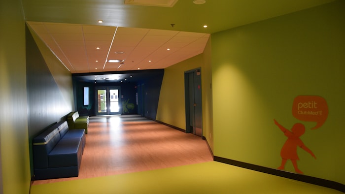 Un couloir coloré menant vers une porte avec des appliqués muraux d'ombres d'enfants sur le mur