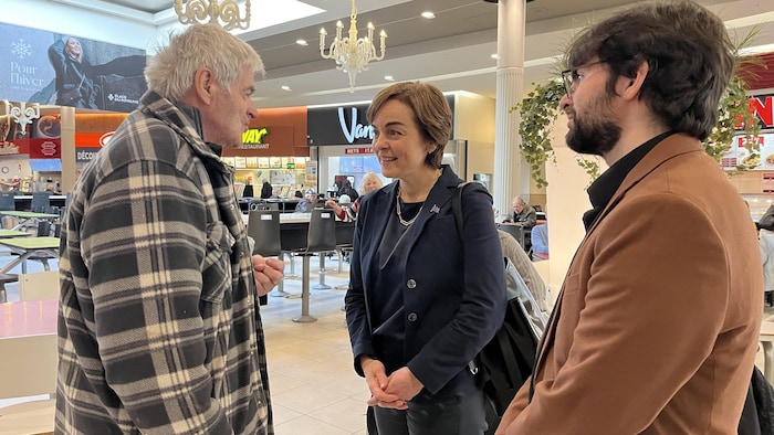 Deux politiciens discutent avec un citoyen dans un centre commercial.
