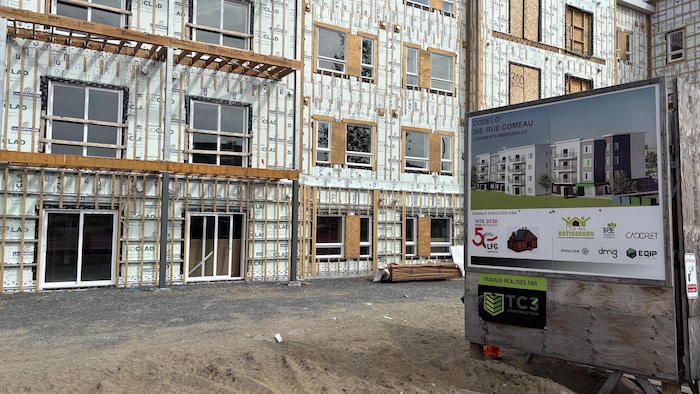Un immeuble en construction recouvert de panneaux isolants se dresse devant un panneau d'affichage du projet.