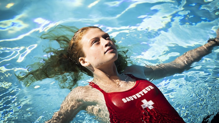 Une jeune fille en maillot de sauveteur nage sur le dos, les yeux levés vers le ciel. 