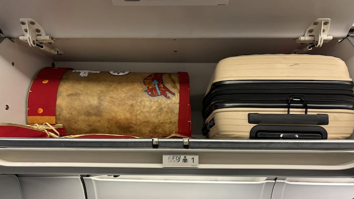 Un casier d'avion en classe affaires ouvert dans laquelle se trouve une valise et le sac contenant la coiffe.