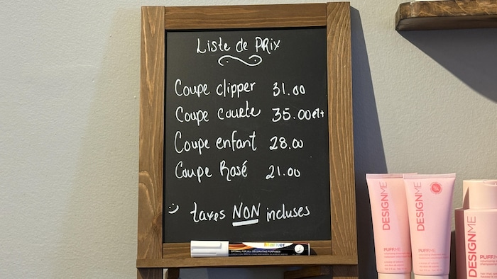 Ardoise affichant les prix d'un salon de coiffure. Aucun prix n'est associé à un genre en particulier.