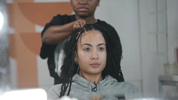 Amala Hutchison-Jones regarde son reflet dans un miroir pendant qu'elle se fait tresser par une coiffeuse