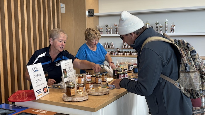 À l'intérieur d'un terminal lumineux avec des murs en bois, deux femmes font une démonstration de pots de confiture sur une table.