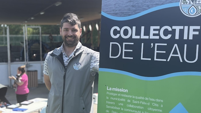 Un homme pose à côté d'une affiche.