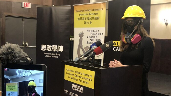Cherie Wong porte un casque, un masque à gaz et des lunettes de protection en s'adressant aux journalistes.
