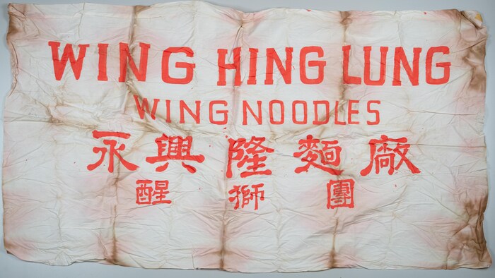 Une bannière en tissu blanc porte des inscriptions en lettres et en caractères rouges.