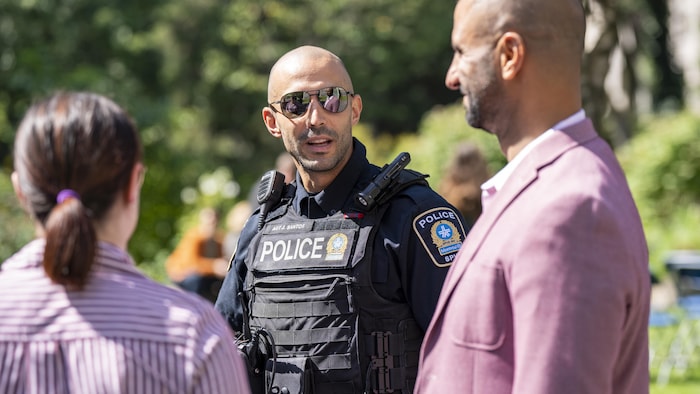 Trois personnes, dont un en uniforme de policier, discutent.